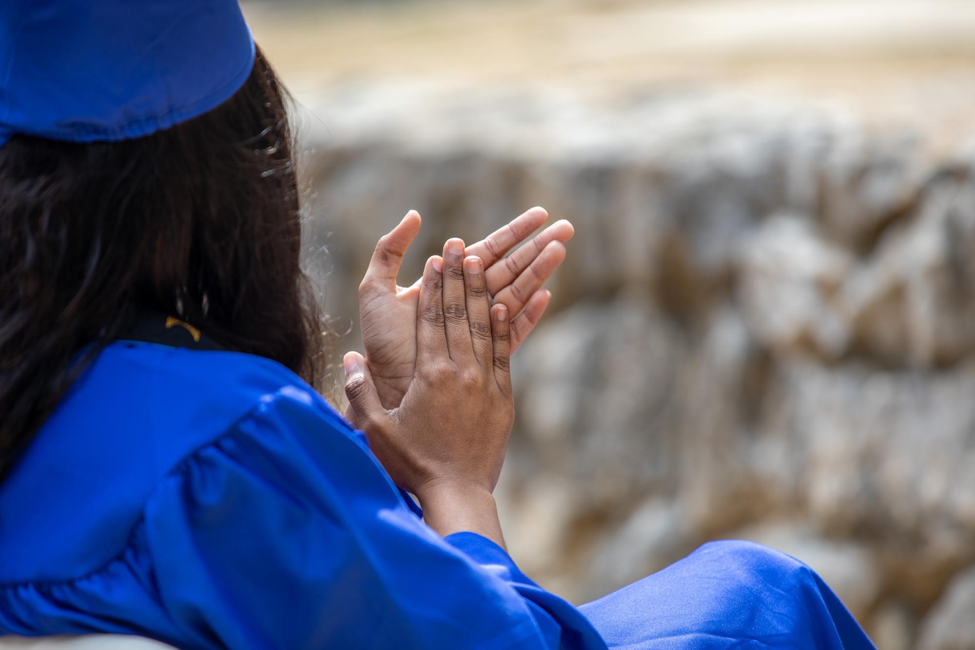 Close-up of a person clapping who is wearing a commencement gown and motarboard.